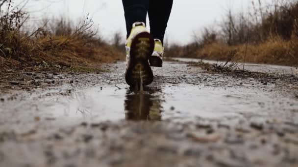 秋天，穿着运动鞋的女人穿着运动鞋跑着跳过水坑，身上撒满了水花和水滴 — 图库视频影像