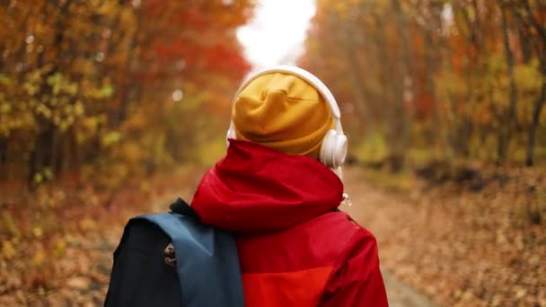 Glada aktiva 50-talskvinna promenader tillsammans med hörlurar mobiltelefon och ryggsäck njuter av att lyssna på musik utomhus i höstens stadspark eller skog bakgrund. — Stockvideo
