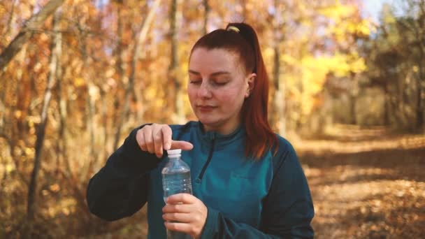활발히 뛰고 있는 활발히 달리는 소녀는, 가을 공원에서 조깅을 하면서 몸을 돌보고 나서 물을 마신다 — 비디오