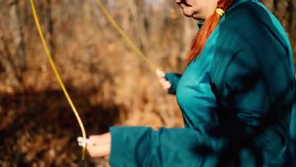 Spor yapan kadın, sonbahar güneşli ormanı boyunca spor kıyafetiyle atlama halatıyla antrenman yapıyor. — Stok video