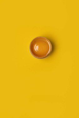 Taze Paskalya. Sarı arka planda yumurta sarısı kırılan kahverengi tavuk yumurtası. Asgari Paskalya konsepti, negatif alan.