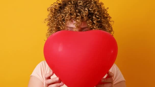 Felice donna caucasica positiva che tiene palloncino a forma di cuore rosso divertirsi isolato su sfondo rosa. Festa di compleanno — Video Stock