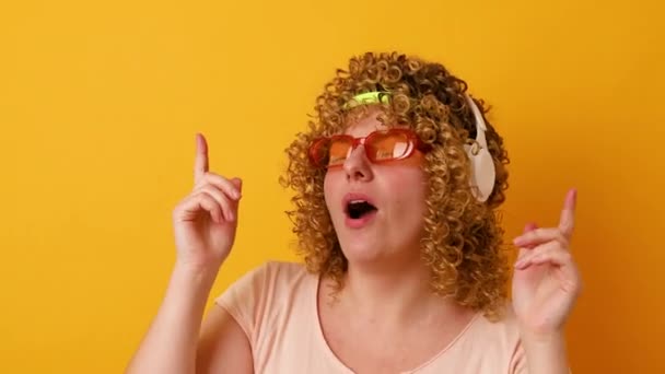 Vicces vidám hullámos hajú lány szemüveggel és egy kötés hallgat lélek tánc szórakozás elszigetelt sárga szín háttér — Stock videók