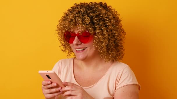 4k 입니다. 밝은 코카서스 행복 한 30 대 여성 곱슬머리에 휴대 전화 스마트폰을 들고 노란색 배경 스튜디오에서 대화를 나누는 모습. — 비디오