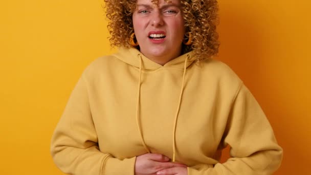 Mujer bastante joven que sufre dolor de estómago, dolor de menstruación sobre fondo amarillo de la pared. — Vídeos de Stock