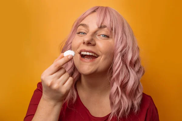 黄色い壁の背景に白いマシュマロを手にした幸せな女性。お菓子・菓子・食のコンセプト — ストック写真