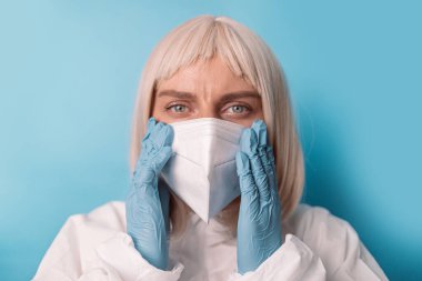 Eldivenli beyaz kadın doktor portresi mavi arka planda n95 tıbbi maske takıyor.