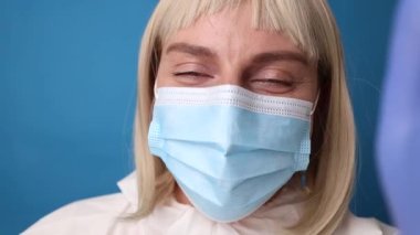 Kadın doktor, klinikte cep telefonuyla açık mavi arkaplan üzerinde video konferansı yapıyor.