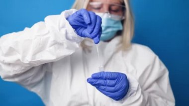 Coronavirus PCR testi. Koruyucu giysi maskeli doktor mavi arka planda teşhis amaçlı tükürük örneği tutan eldiven.