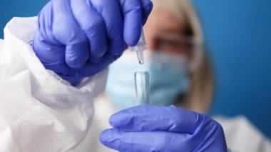 Coronavirus PCR testi. Koruyucu giysi maskeli doktor mavi arka planda teşhis amaçlı tükürük örneği tutan eldiven.