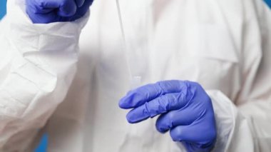 Koruyucu giysi maskeli doktor mavi arka planda teşhis amaçlı tükürük örneği tutan eldiven.