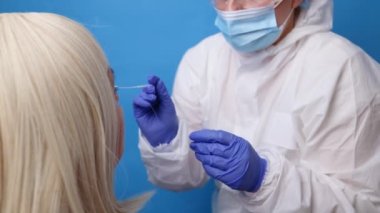 Tıbbi PPE kıyafetli doktor mavi arka planda Coronavirüs için Coronavirus covid-19 antijen testine hastanın burnundan örnek alır.