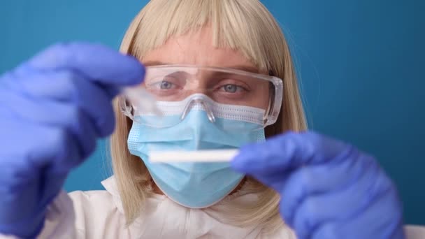 Nahaufnahme eines Arztes im medizinischen PSA-Anzug hält COVID-19 Coronavirus PCR-Test über hellblauem Hintergrund — Stockvideo