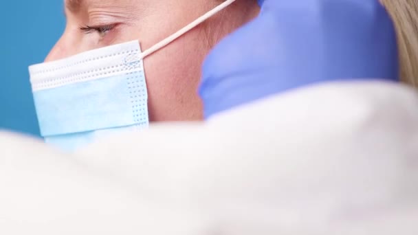 Medico femminile in tuta protettiva guanti maschera medica mettendo maschera per la prevenzione del virus corona sul suo viso su sfondo di colore blu — Video Stock