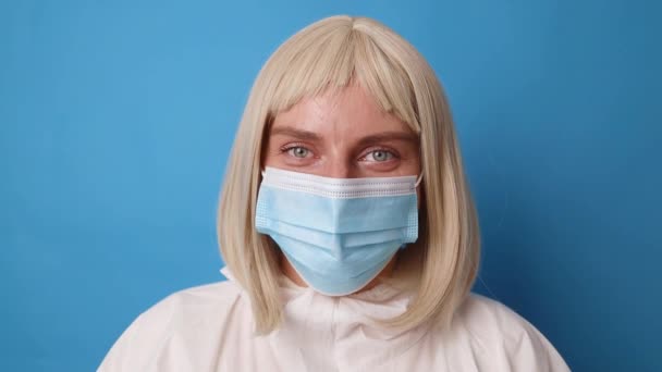 Porträtt av kvinnlig läkare eller sjuksköterska bära blå handskar i medicinsk PPE kostym över ljusblå färg bakgrund på sjukhus — Stockvideo