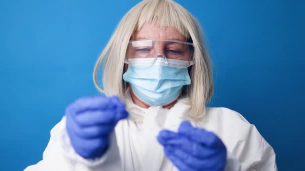 Gros plan du médecin femme en costume PPE médical détient test PCR coronavirus COVID-19 sur fond bleu vif — Video