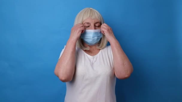 Портрет 60-х женщина снять медицинскую маску из-за ковид на ярко-голубой цвет фона — стоковое видео