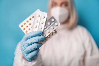 Kadın doktorun kameraya bakarken yüz maskesi takıp elinde antiviral ilaç tutarken Coronavirus covid 19 salgınına karşı.