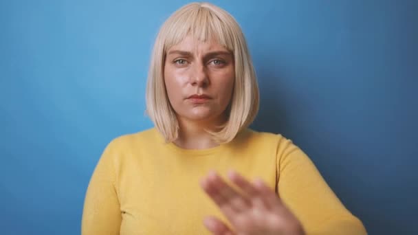 黄色のセーターを交差手で白人女性の肖像画は、停止ジェスチャーを行います,青の背景に孤立拒絶を示しています — ストック動画