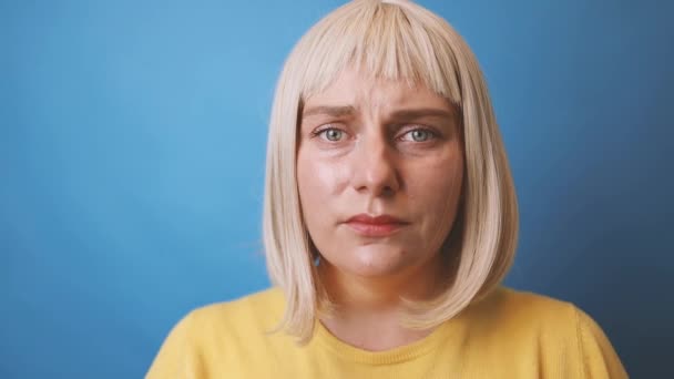 Nærbillede af en ung trist kaukasisk 30 'er kvinde iført gul sweater look kamera isoleret på blå farve baggrundsstudie. – Stock-video