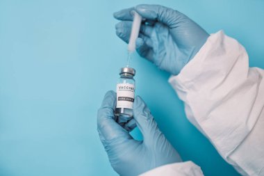 Coronavirus aşısı şişesi ve şırıngası olan bir doktor. Doktor, Covid-19 aşısının üçüncü aşısı için açık mavi arkaplan üzerinde bir doz hazırlıyor.