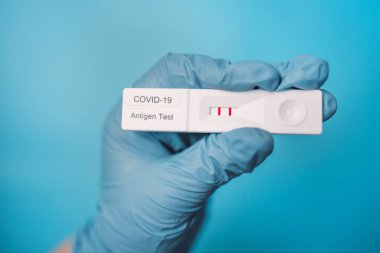 Doktorun elinde pozitif hızlı yanal akış COVID 19 testi açık mavi arka plan üzerinde