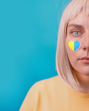 Mavi arkaplanda izole edilmiş kameraya bakan, aşk sembolü ile üzgün beyaz kadın yüzü..