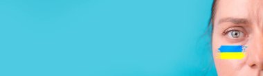 Ukrayna bayraklı, üzgün beyaz kadın yüzü mavi arkaplanda izole edilmiş kameraya bakıyor..