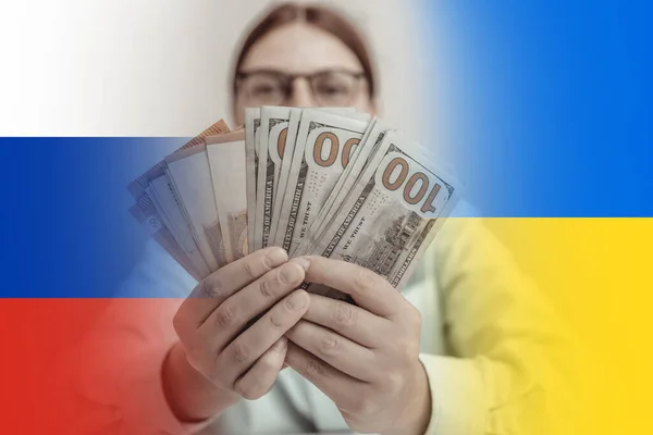 Война на Украине. Грустная деловая женщина, прикрывающая лицо деньгами на фоне синего и желтого флага Украины и российского флага — стоковое фото