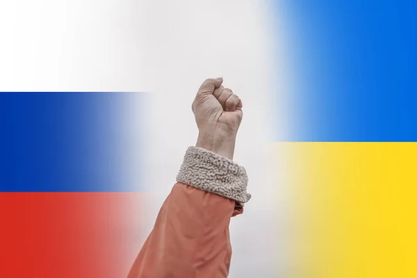 Relações políticas internacionais entre a Ucrânia e a Rússia. Punho levantado contra pano de fundo de bandeiras ucranianas e russas. — Fotografia de Stock
