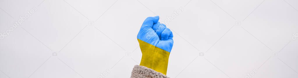 female hand fist painted in Ukraine flag colors yellow-blue against sky. Stop war between Russia and Ukraine. International political relationship between Ukraine and Russia.