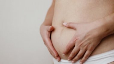 Artı şişman kadın göbeği, selülitleri kontrol etmek için deriyi tutan kadın. Şişman bir karında sarkık deri, gri arka planda plastik cerrahi konsepti