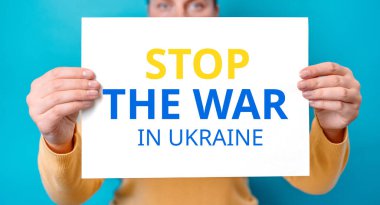 Genç kadın, Ukrayna 'daki savaşı durdurmak için mavi arka planda yarım yamalak afiş yapıştırıyor.