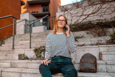 Profesyonel giyinen genç sarışın iş kadını akıllı telefon kullanarak şehire gülümsüyor.