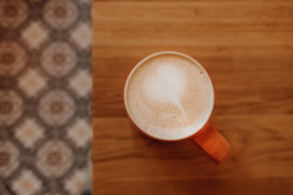 Kaffee in einer orangefarbenen Tasse auf einem Holztisch in einem Café. FLAT LAY — Stockfoto
