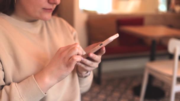 Primer plano de las manos de la mujer utiliza teléfono inteligente sentado en la mesa en la cafetería — Vídeo de stock