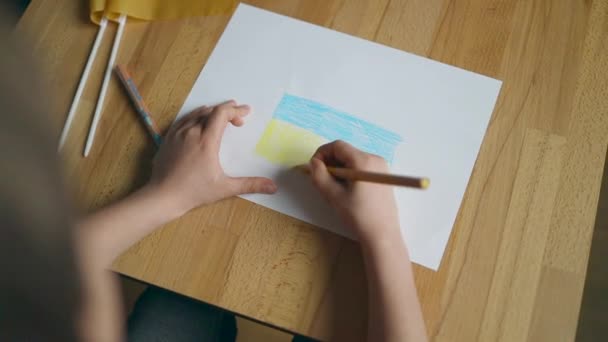 Kinderen handen met gele en blauwe kleur potlood tekening van de Oekraïense vlag indoor thuis — Stockvideo