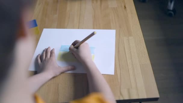 Kinderen handen met gele en blauwe kleur potlood tekening van de Oekraïense vlag indoor thuis — Stockvideo