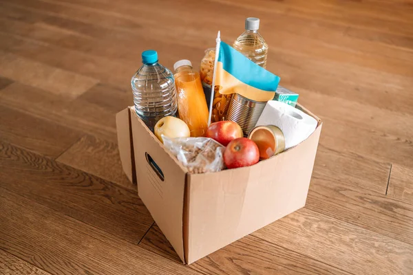  Ukraynalı çocuklar ve kapıdaki ahşap zemindeki insanlar için farklı market ürünlerinin olduğu kağıt dolu bir bağış kutusu. Ukrayna Bağışı. Gönüllü olmak, bağışta bulunmak, yardım amaçlı mülteciler, savaş..