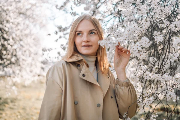 Çiçek açan bahar bahçesinde kokunun tadını çıkaran genç bir kadının portresi. Seyahat, özgürlük ve bahar tatili.