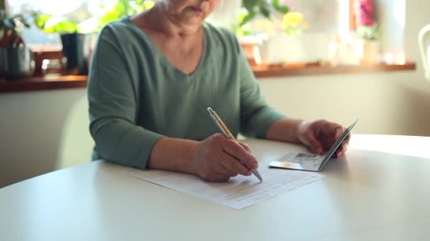 50 кавказская женщина 60-х годов пишет ручкой в документе PESEL на белом столе в департаменте госслужбы — стоковое видео