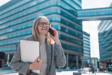 İş merkezinin önünde yürürken cep telefonuyla konuşan kendinden emin bir kadın.