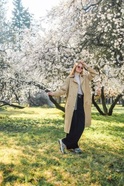 Şık giyinen mutlu bir kadının portresi. İlkbaharda pembe çiçeklerin arasında eğleniyor.. 