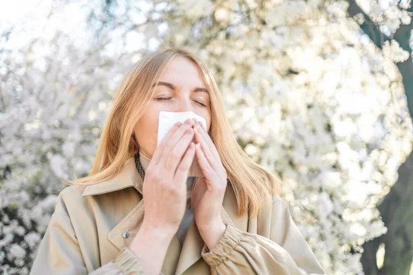 Bahar polen alerjisi yüzünden hapşıran mendili olan genç bir kadın, açık havada mevsimsel alerji.