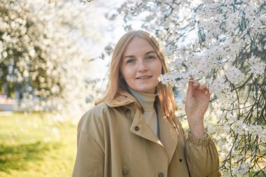 Çiçek açan baharda kokunun tadını çıkaran genç bir kadın. Seyahat, özgürlük ve bahar tatili. Moda tarzı.
