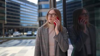 Yaratıcı iş kadını şık kıyafetler giyiyor. Çatı katındaki ofis binasının yanında akıllı telefon kullanıyor.