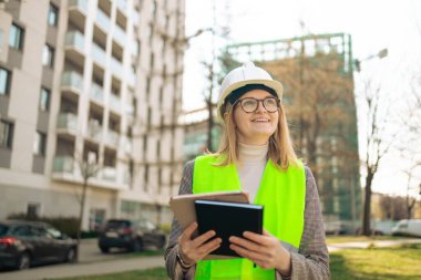Tablet ve not defteri olan mutlu kadın mühendis inşaat alanında duruyor, çalışıyor.. 