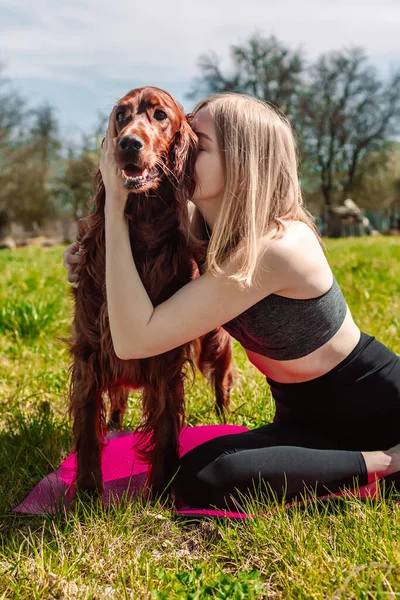 Young blonde girl is doing yoga on the grass with beautiful Irish Setter dog — Photo