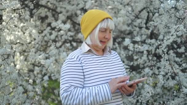 Beautiful attractive smiling 50s woman holding using smartphone posing in spring time — Stock Video