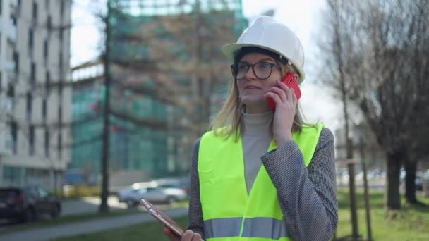 努力工作的女建筑工程师站在建筑工地上.自信的工程师在电话上交谈，展示正在进行的外壳工作 — 图库视频影像